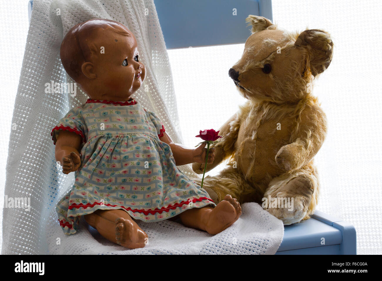 Vintage poupée céramique offrant une apparence rose rouge frais à un ours en peluche sur une couverture blanche sur une chaise bleue. Fond blanc Banque D'Images