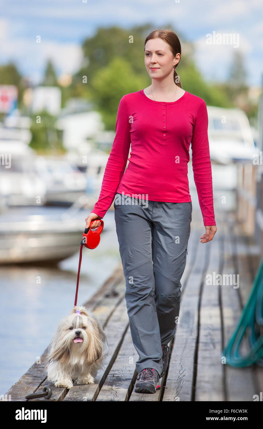 Jeune femme avec shih-tzu dog walking sur town quay avec les bateaux. Banque D'Images