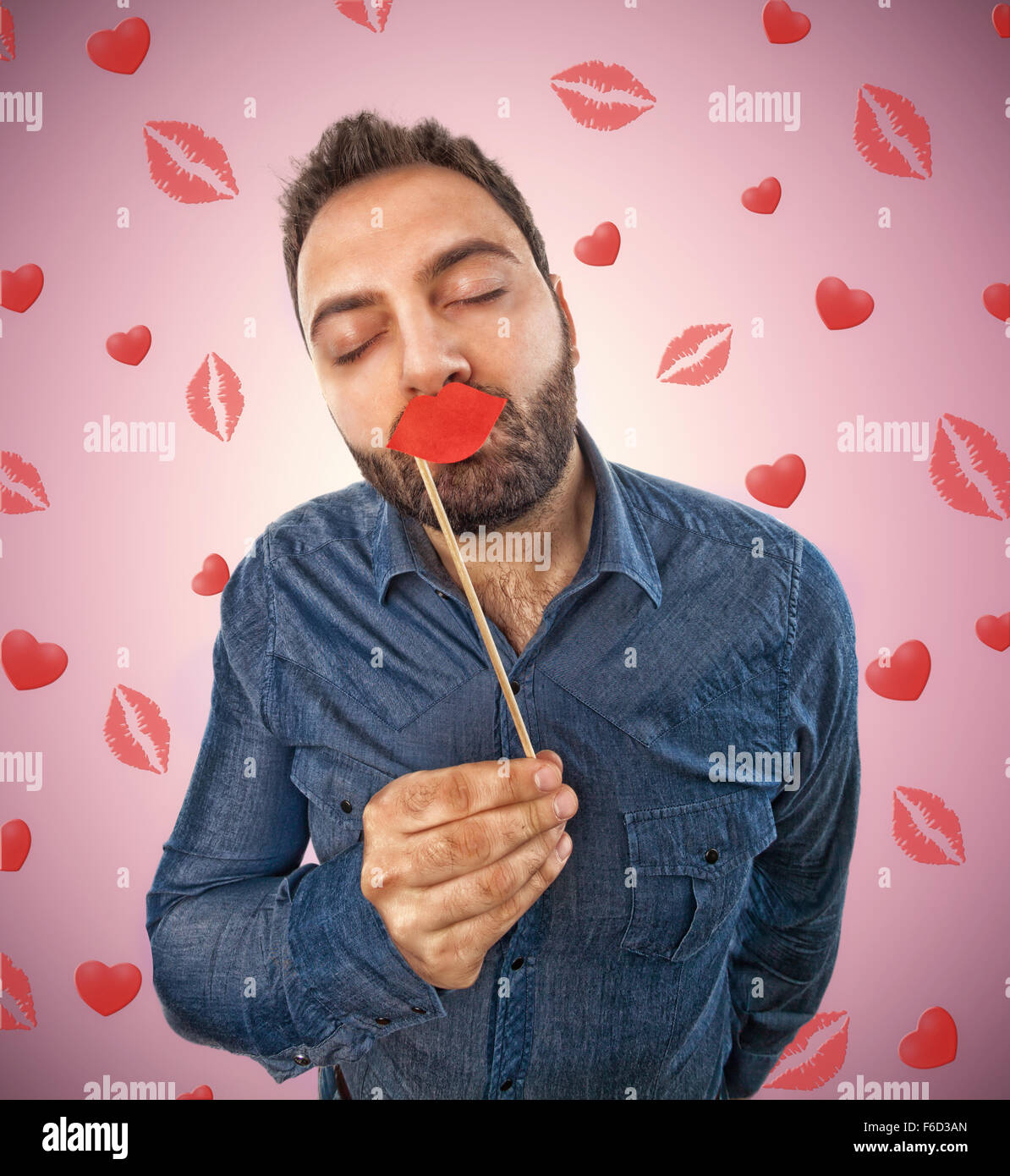Jeune homme avec Photo Booth et l'arrière-plan en forme de lèvres de baisers et les cœurs Banque D'Images
