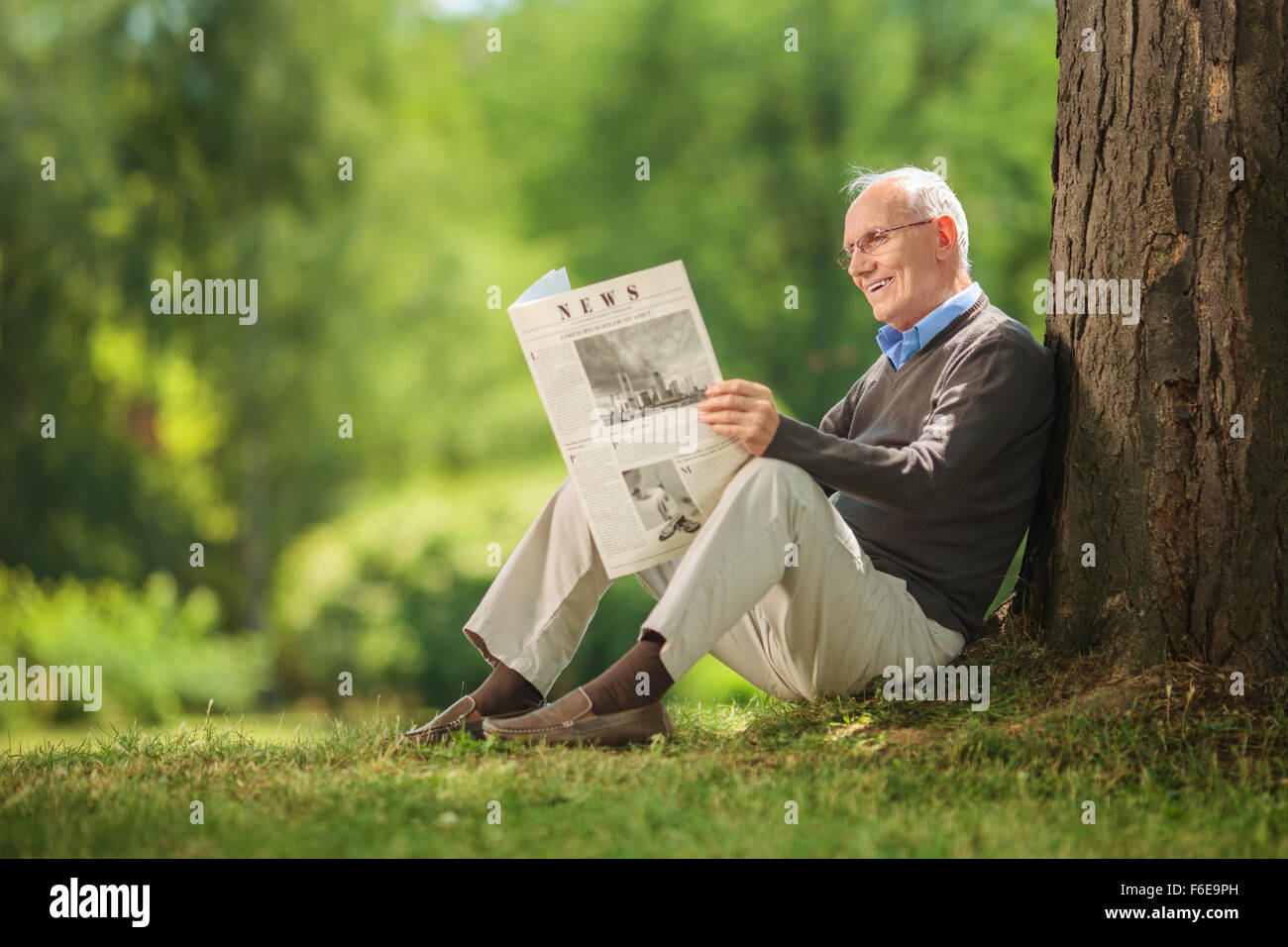 La haute atmosphère assis par un arbre dans un parc et la lecture d'un journal sur une belle journée ensoleillée Banque D'Images