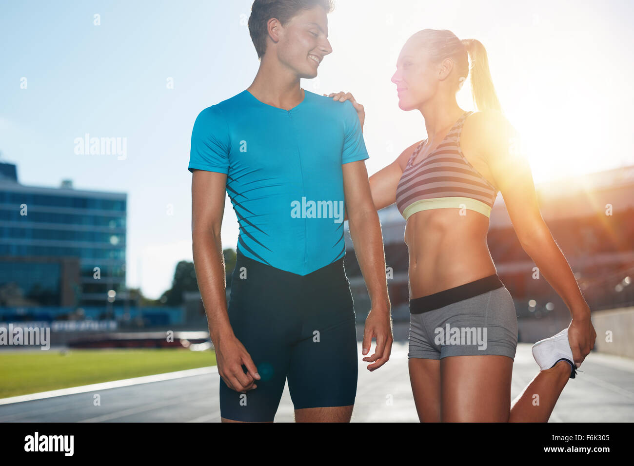 Young runner s'étendant ses jambes devant un track event. Deux jeunes coureurs sur une journée ensoleillée pratiquant à stade de l'athlétisme. Banque D'Images