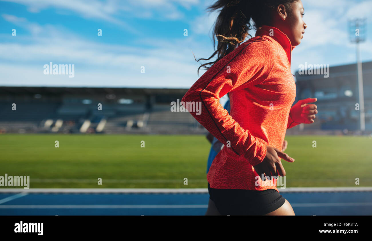 Vue de côté de l'ajustement jeune femme en cours d'exécution. La formation de l'athlète féminine de l'Afrique sur la voie de course au stade de l'athlétisme. Banque D'Images Vue de côté de l'ajustement jeune femme en cours d'exécution. La formation de l'athlète féminine de l'Afrique sur la voie de course au stade de l'athlétisme. Banque D'Images