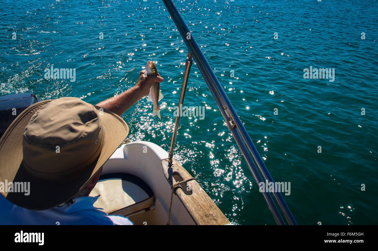 Pêcheur dans le bateau avec bar en sa main Banque D'Images