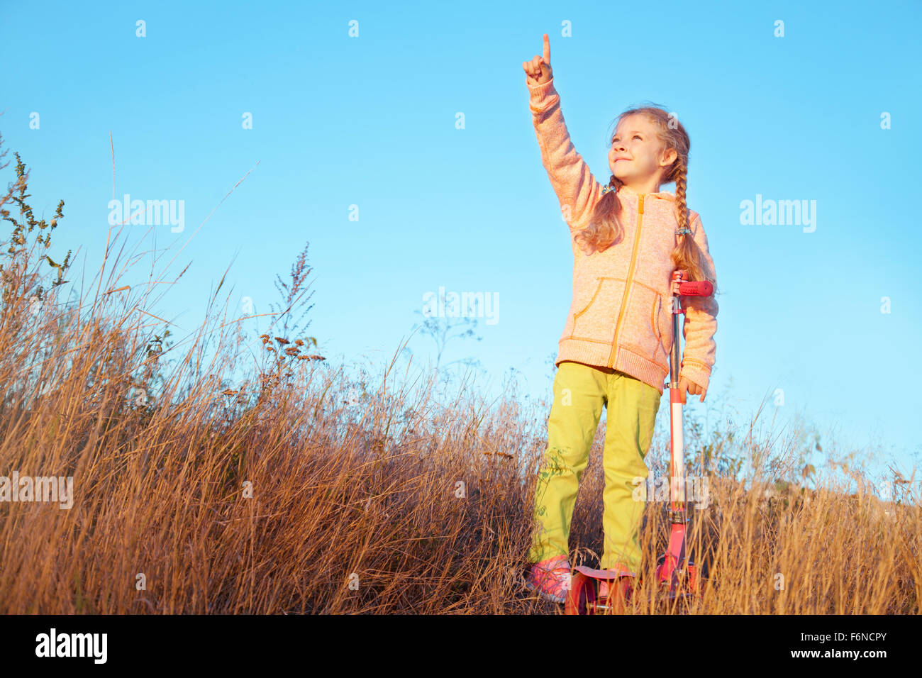 Petite fille dans des vêtements avec scooter montre un doigt vers le ciel sur la nature Banque D'Images