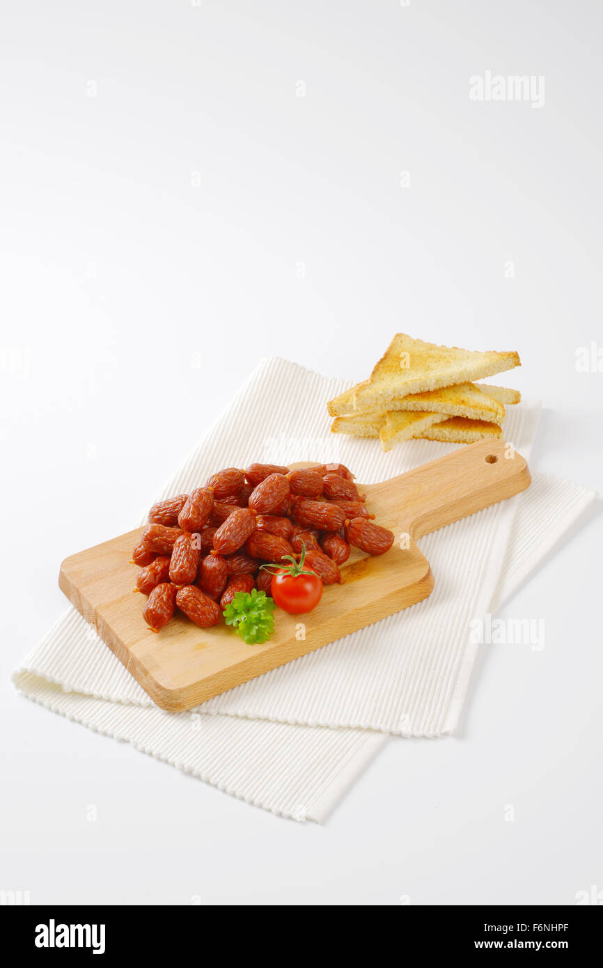 Chaîne de mini saucissons sur planche à découper en bois et blanc set de table Banque D'Images