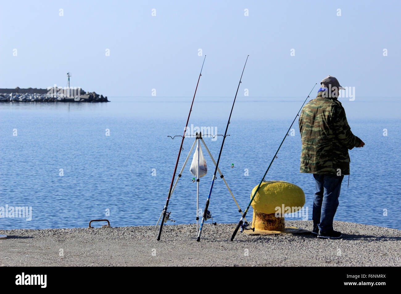 Des cannes à pêche sur leurs titulaires/ stands et un pêcheur amateur debout à la mer du vieux port de Myrina. L'île de Lemnos, GR Banque D'Images