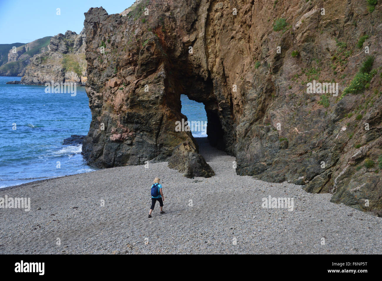 Femme seule se dirigeant vers une arche naturelle dans la falaise de grès sur Dixcart Bay, Sark, Channel Islands. Banque D'Images