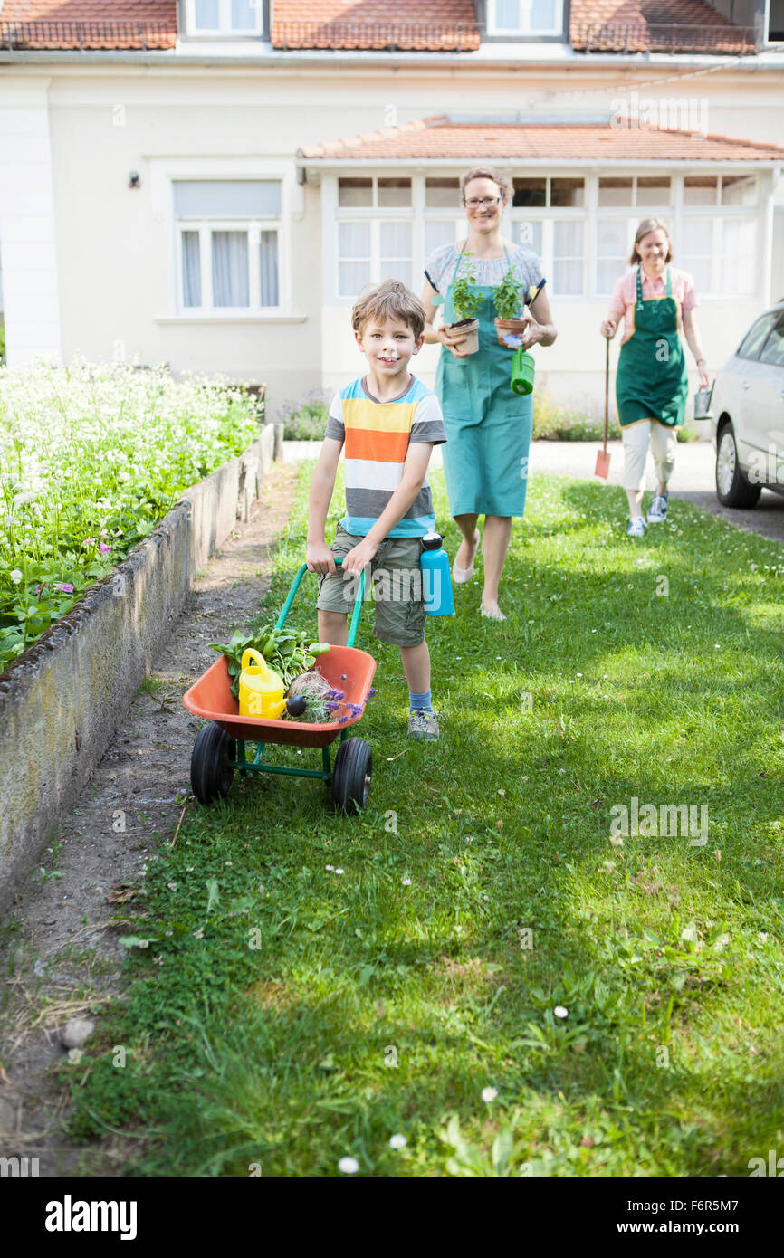 Boy pushing wheelbarrow avec des plantes dans le jardin de légumes Banque D'Images