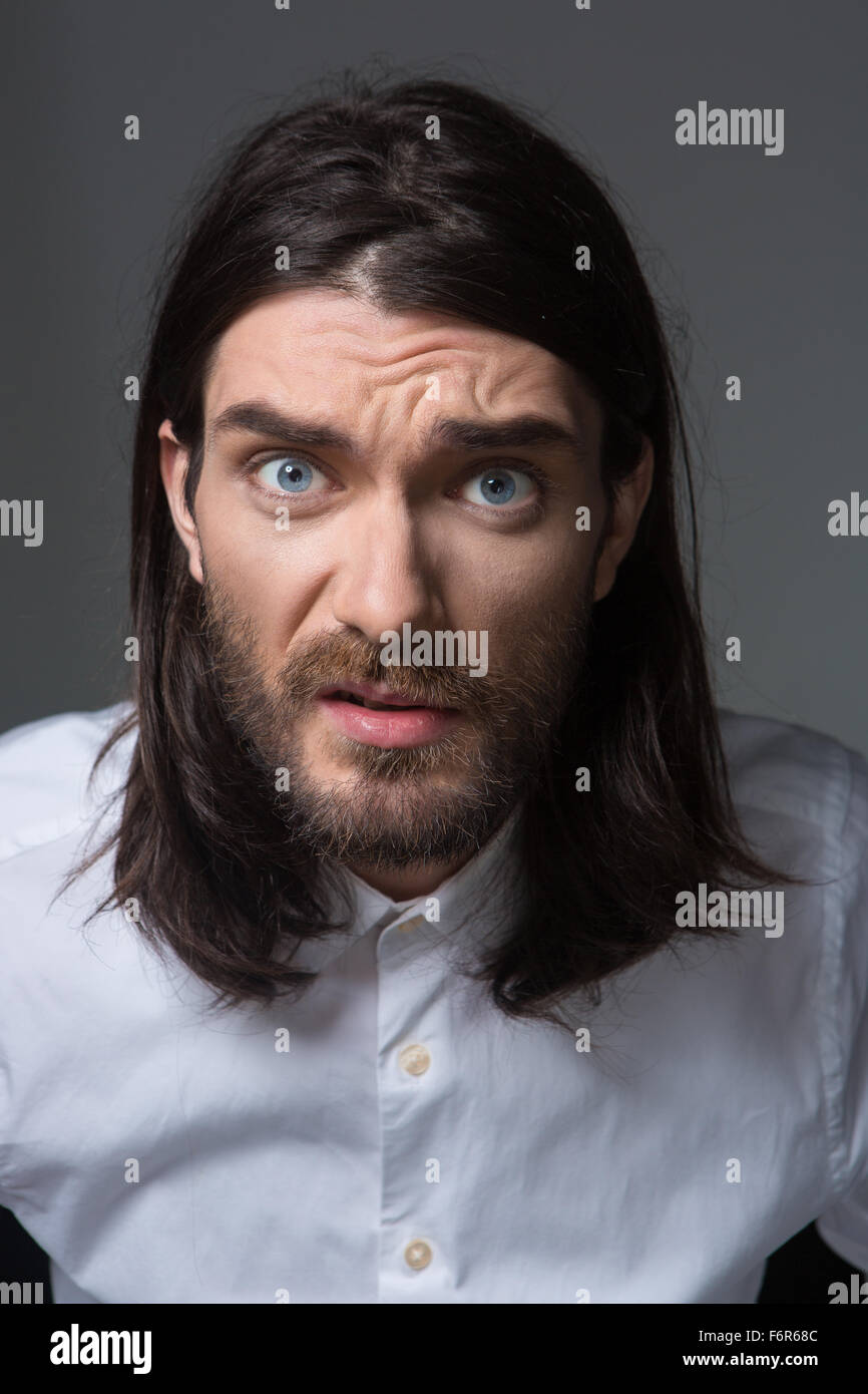Portrait d'un jeune homme en colère avec barbe et cheveux longs à la caméra à l'isolé sur un fond noir Banque D'Images