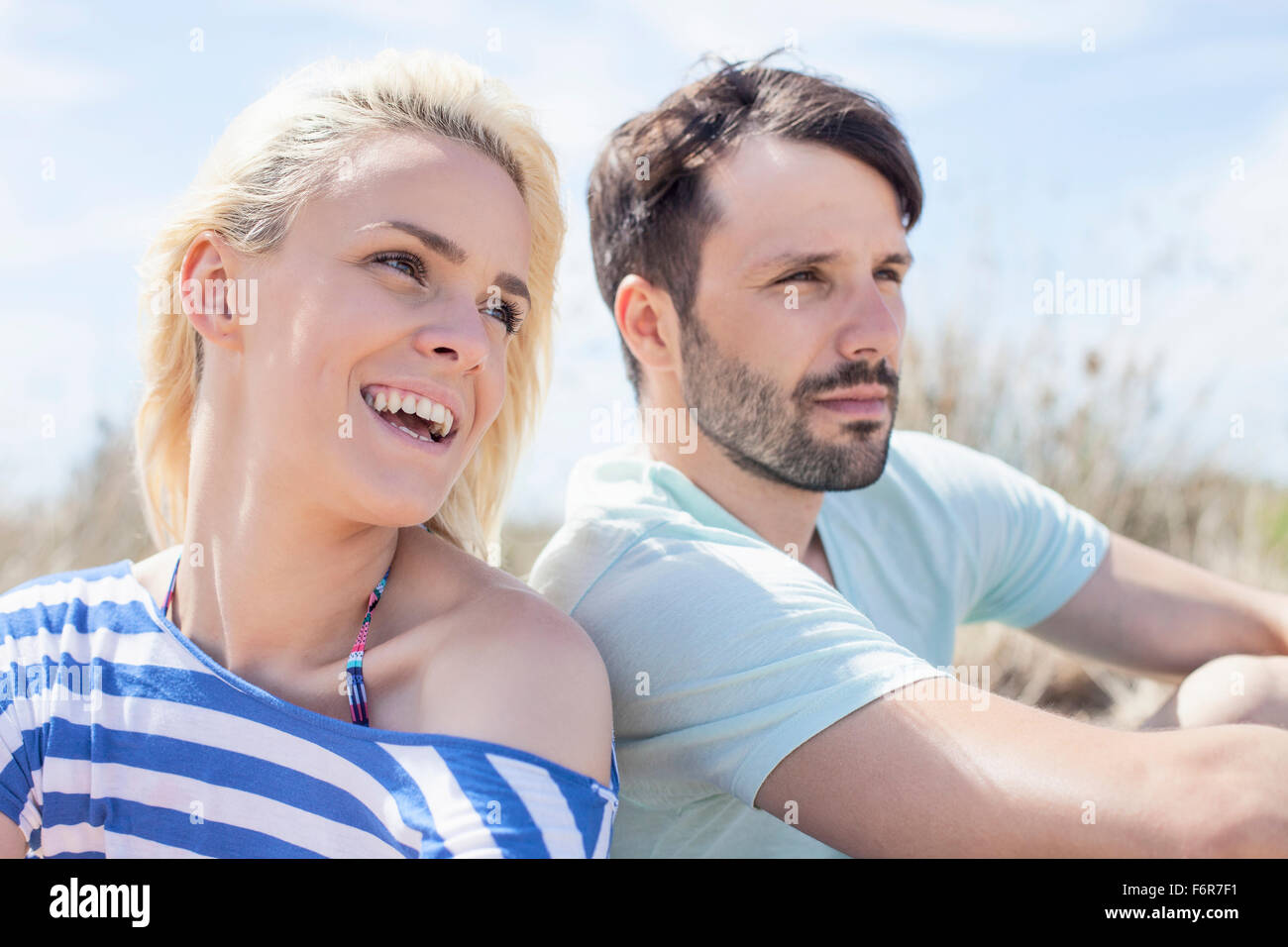 Jeune couple assis côte à côte sur la plage Banque D'Images