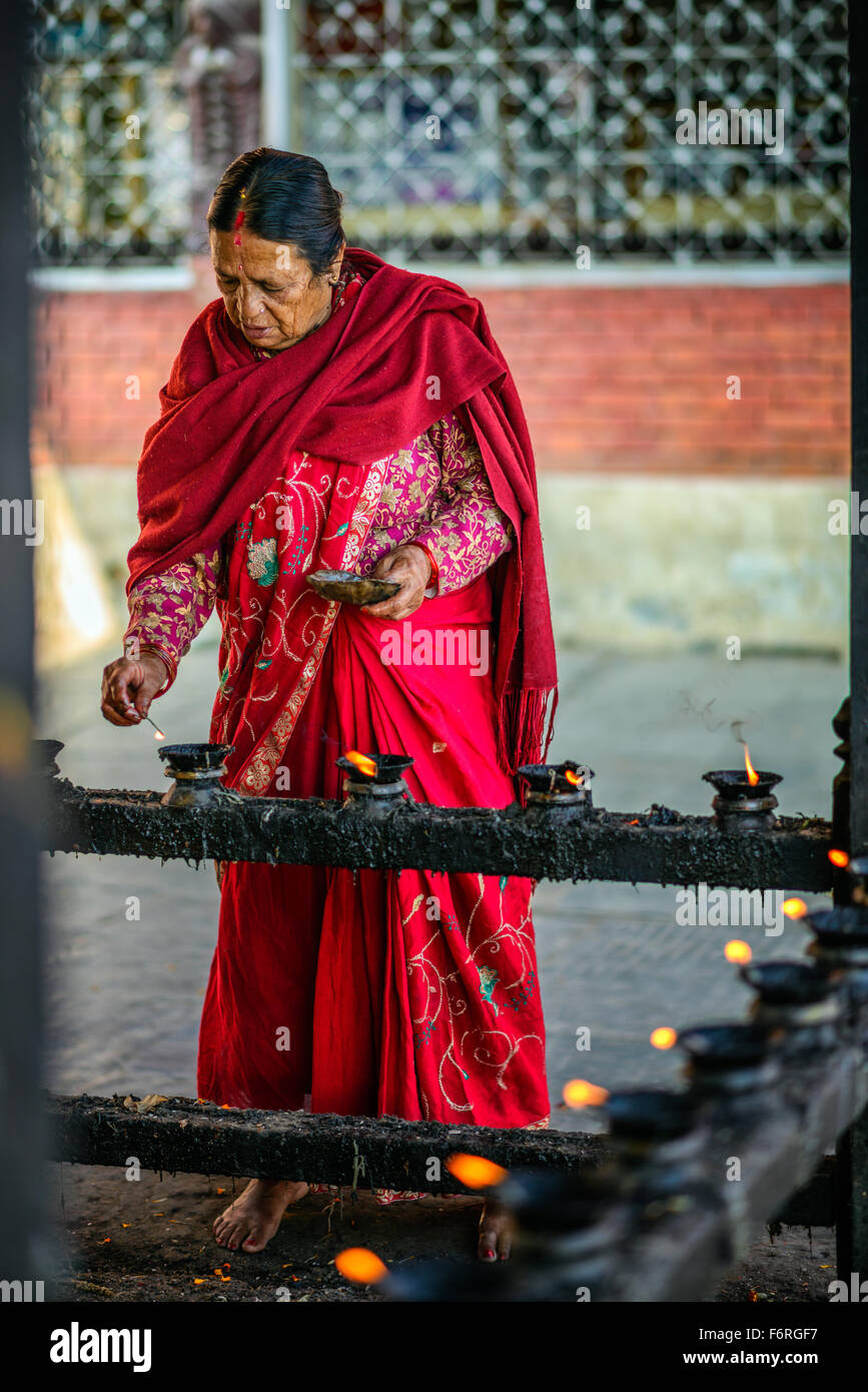 Femme âgée allumant des bougies avant la prière dans un temple à Katmandou Banque D'Images