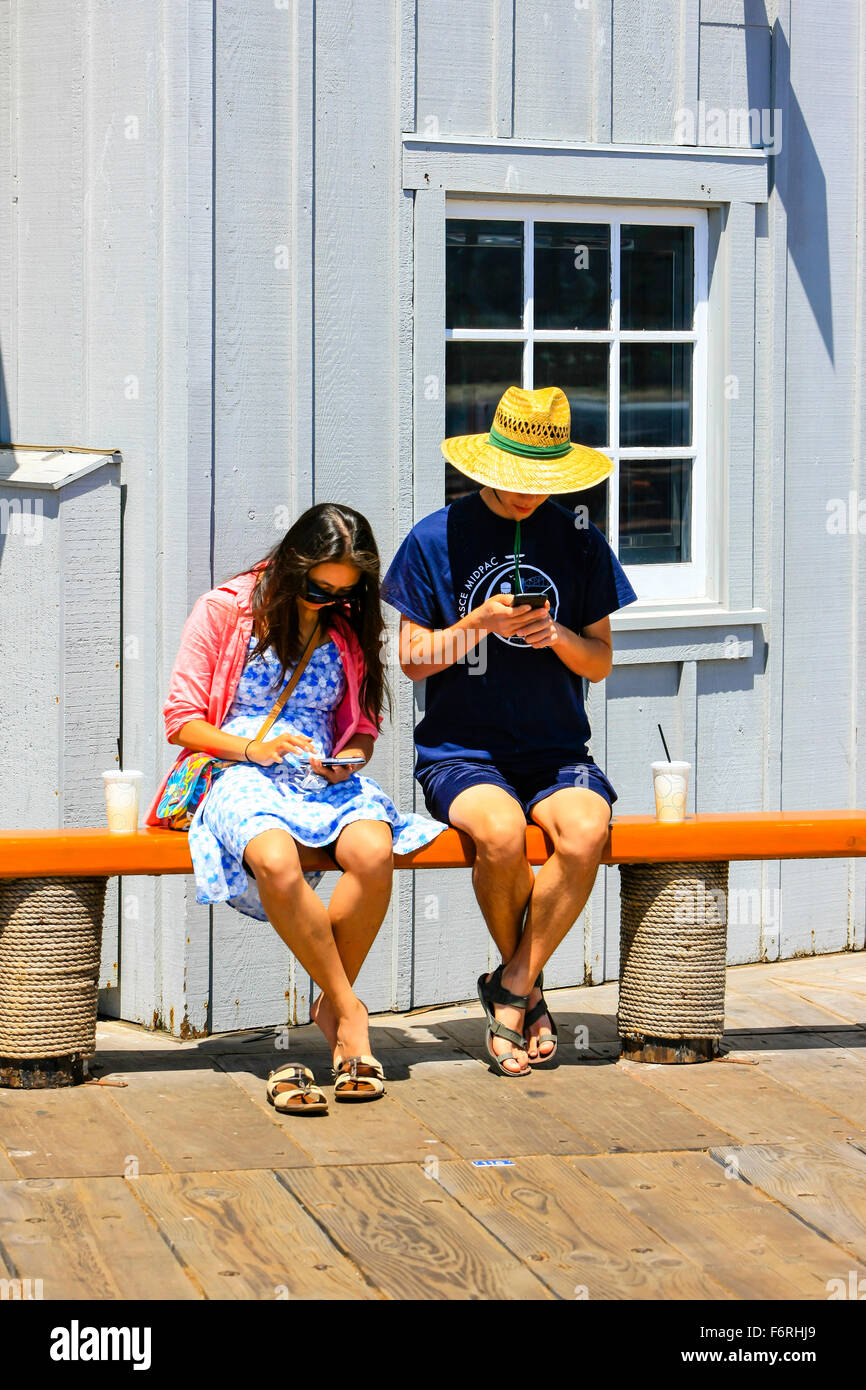 Deux personnes assis sur une banquette en interaction avec leur cellulaire mais ignorer les uns les autres Banque D'Images