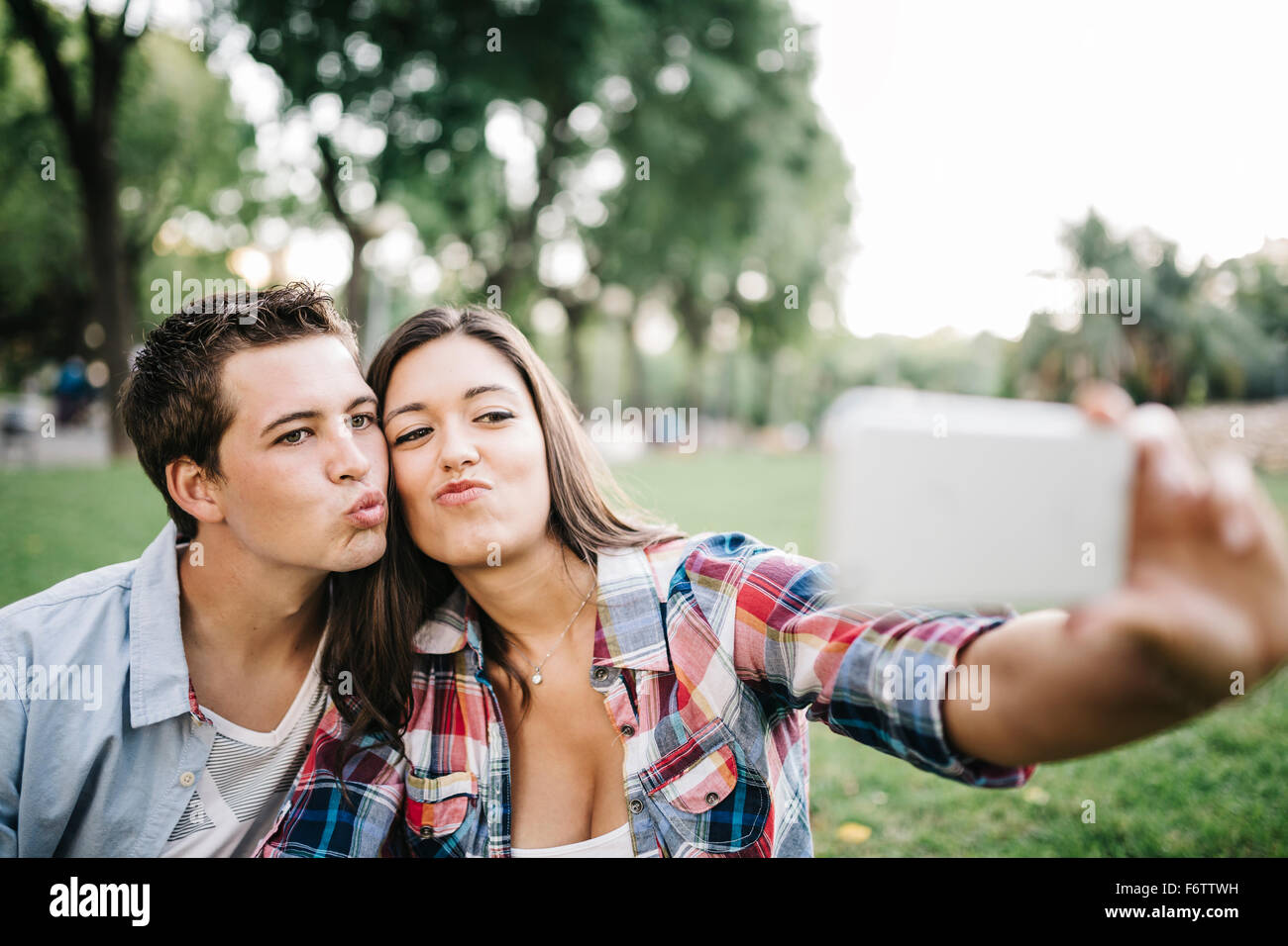 Portrait of young couple in love en tenant un smartphone avec selfies dans un parc Banque D'Images