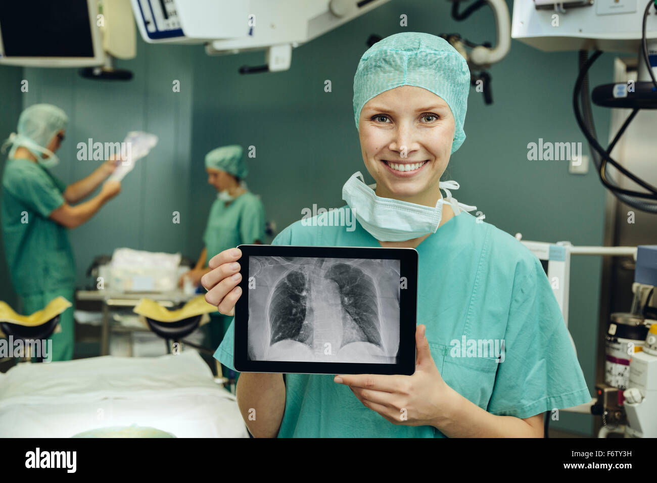 Female chirurgien en salle d'opération tenant une tablette numérique avec un thorax x-ray image Banque D'Images