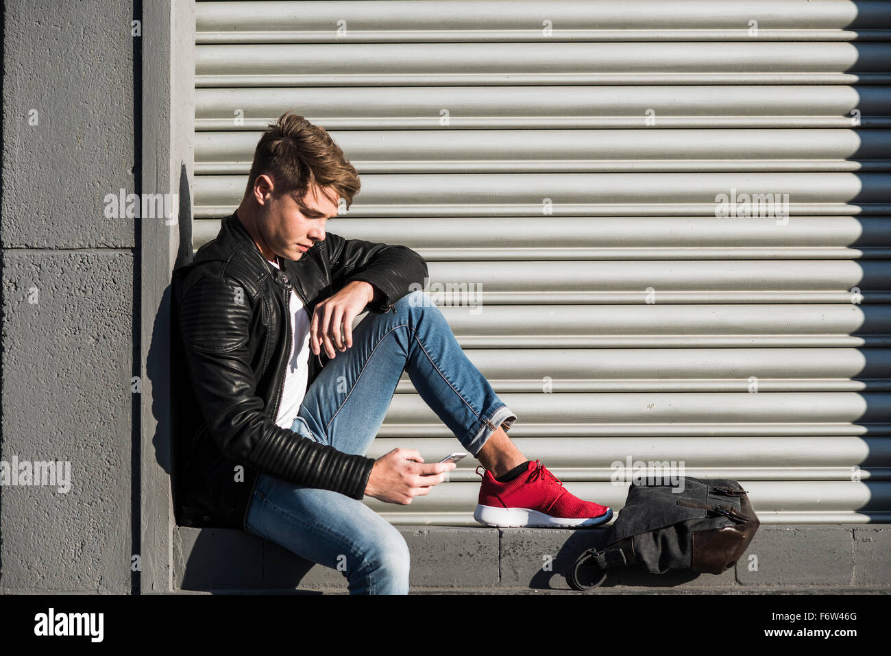 Jeune homme assis dans une niche looking at cell phone Banque D'Images