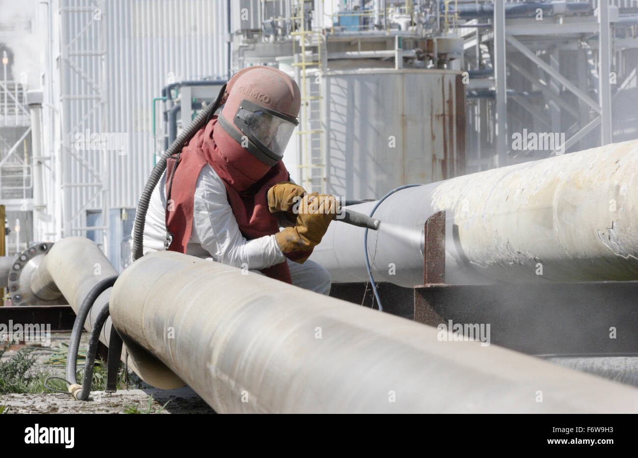 Un travailleur utilise un jet haute pression pour nettoyer les tuyaux de la pétrochimie Banque D'Images