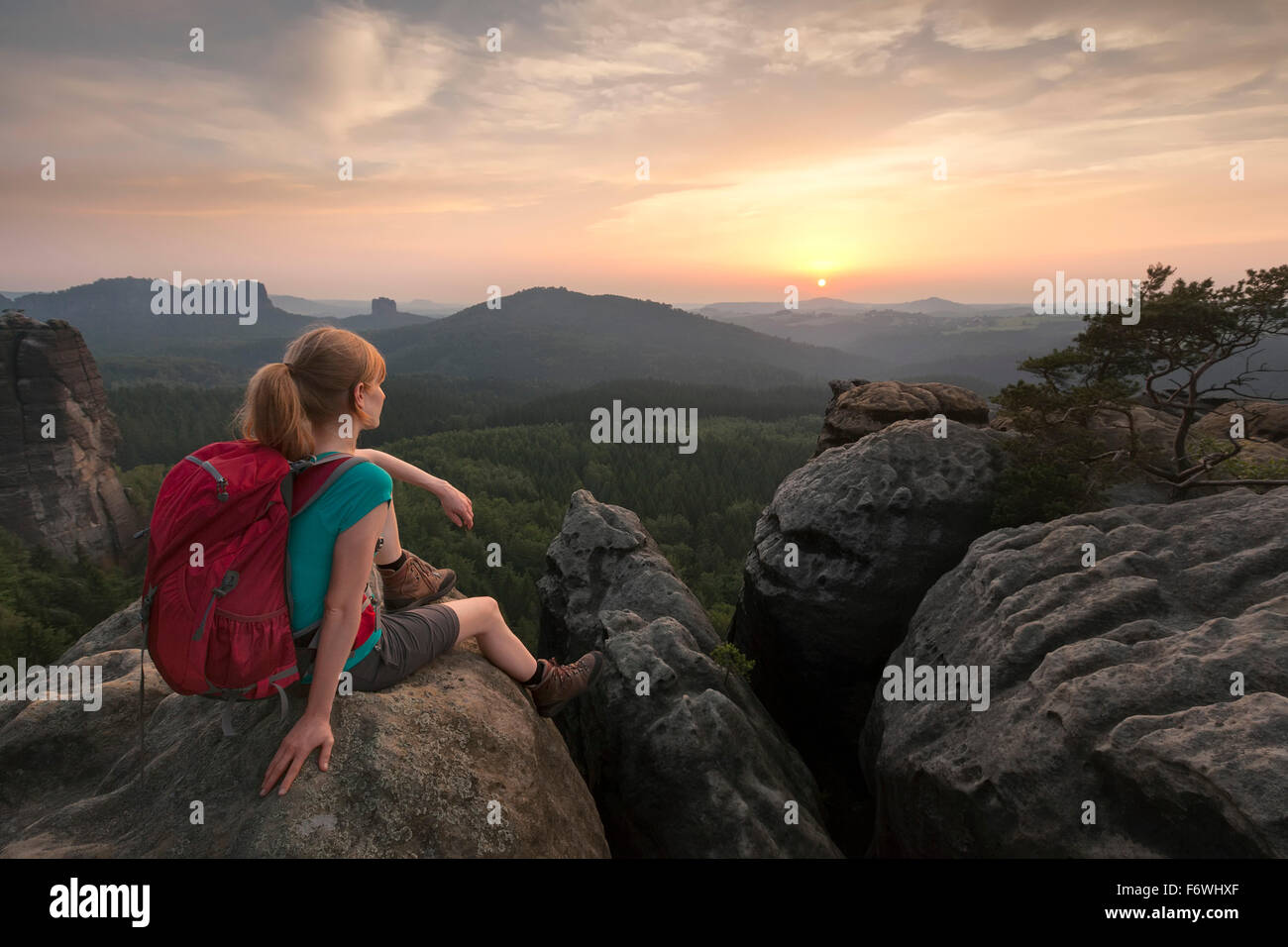 Jeune femme assise sur un rocher tout en admirant le coucher du soleil, Parc National de la Suisse Saxonne, Saxe, Allemagne Banque D'Images