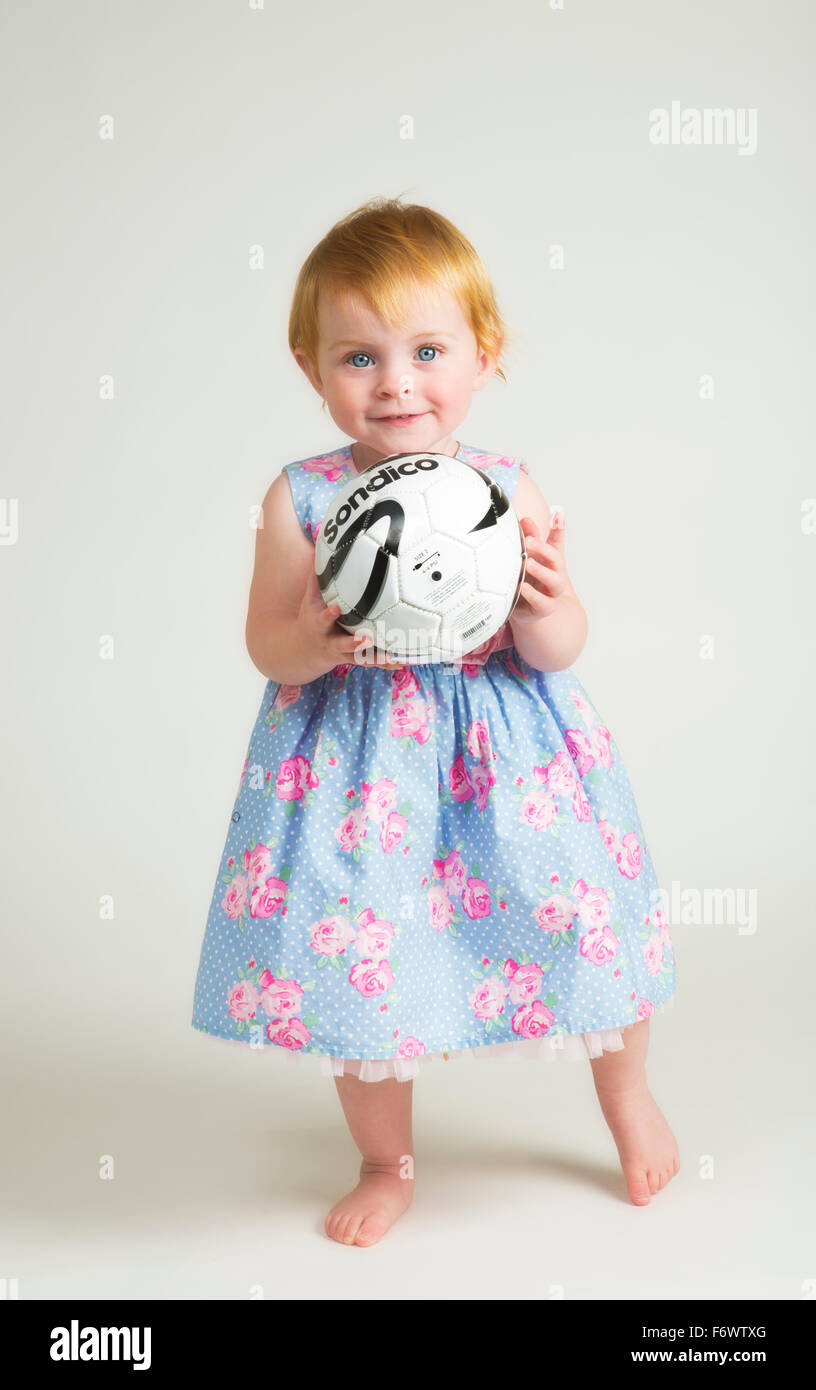 Une jolie petite fille de un an dans une robe tenant un foot ball Banque D'Images