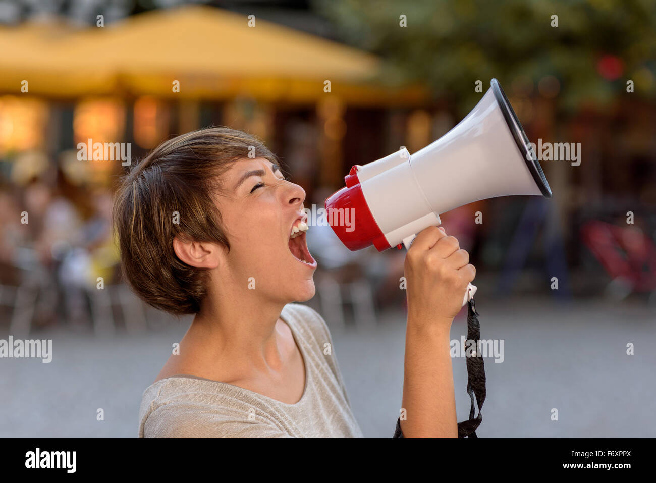 Jeune femme en colère crier dans un mégaphone comme elle se tient sur une rue urbaine ses frustrations d'évacuation lors d'un rassemblement en plein air Banque D'Images