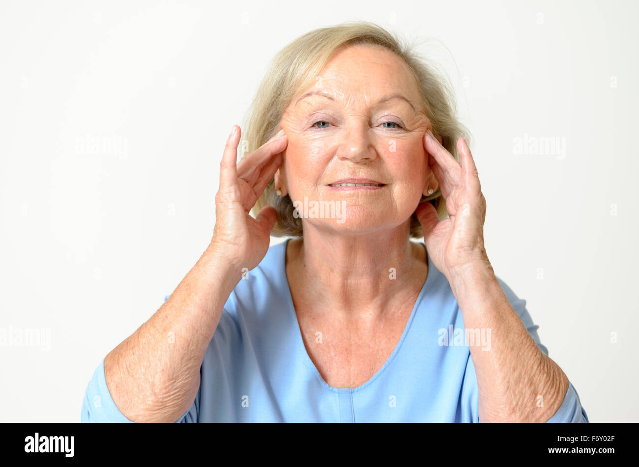 Senior woman wearing blue shirt tout en montrant son visage, effet du vieillissement causé par la perte d'élasticité, close-up Banque D'Images