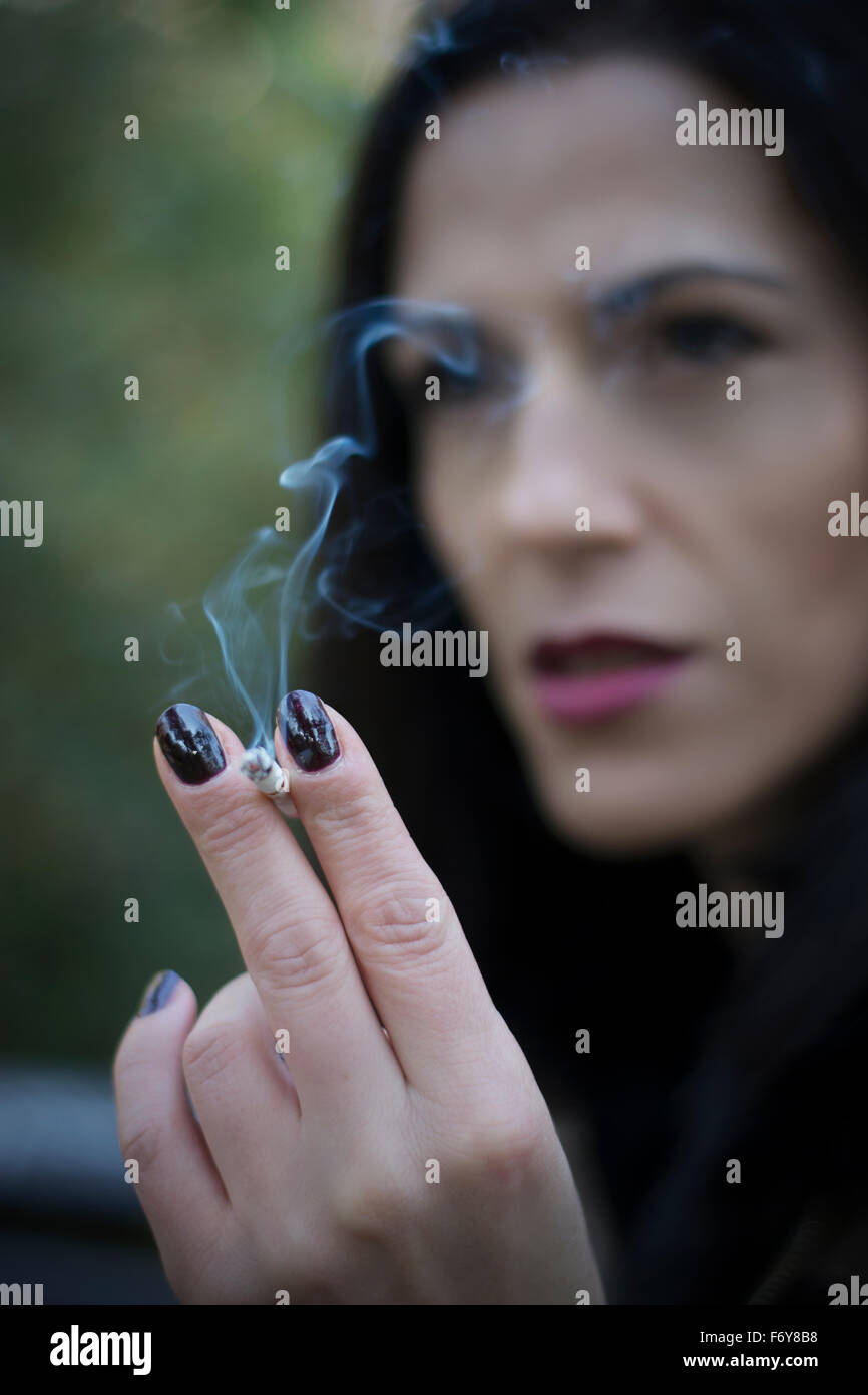 Belle black hair woman enjoying cigarette dans park Banque D'Images