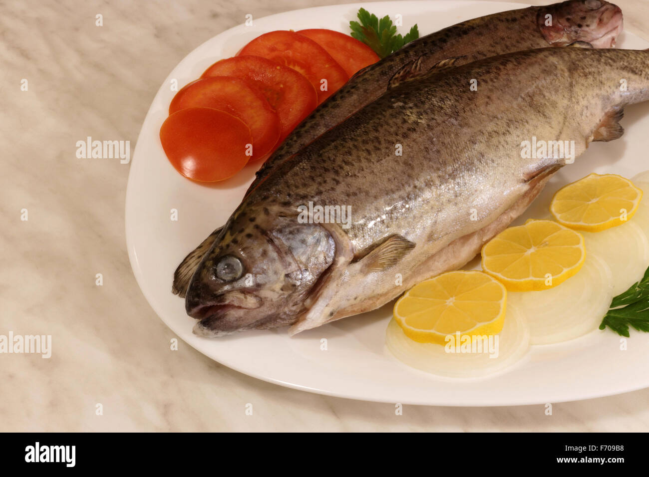 Deux matières trouts sur plaque blanche avec des tomates, le persil, le citron et l'oignon Banque D'Images