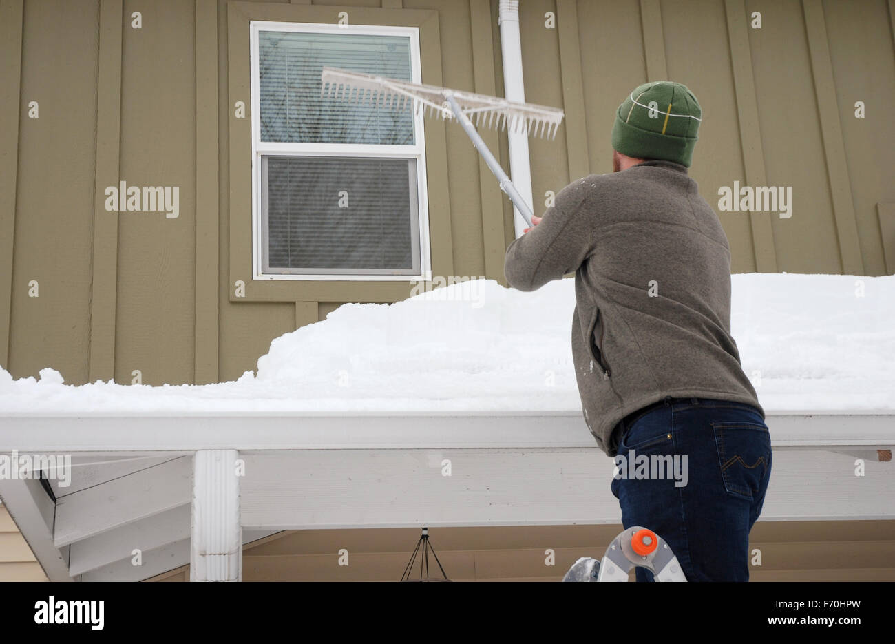 Caucasian man using râteau pour pelleter la neige lourde off roof Banque D'Images