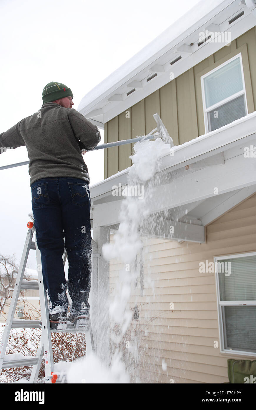 Caucasian man using râteau pour pelleter la neige lourde off roof Banque D'Images