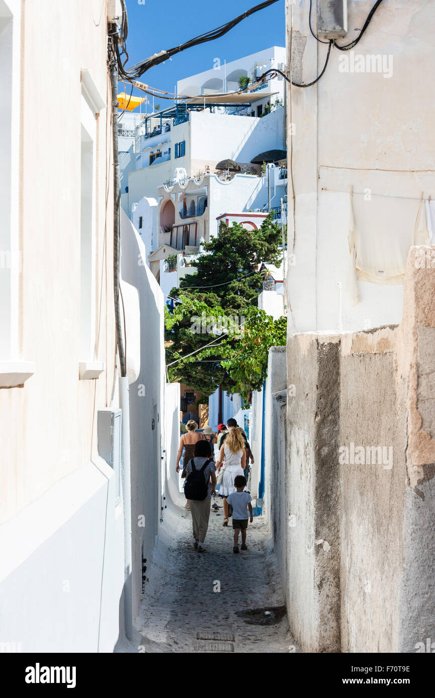 Santorin. Les touristes en se promenant dans la rue pavées typiques avec de grands murs blancs sur les deux faces, dans le vieux centre-ville de Fira. Banque D'Images