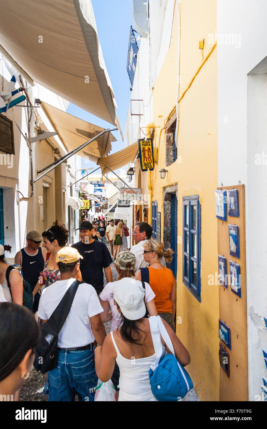 Santorin. Les touristes en se promenant dans la rue pavées typiques avec des magasins des deux côtés, et les frais généraux, les stores dans le vieux centre-ville de Fira. Banque D'Images