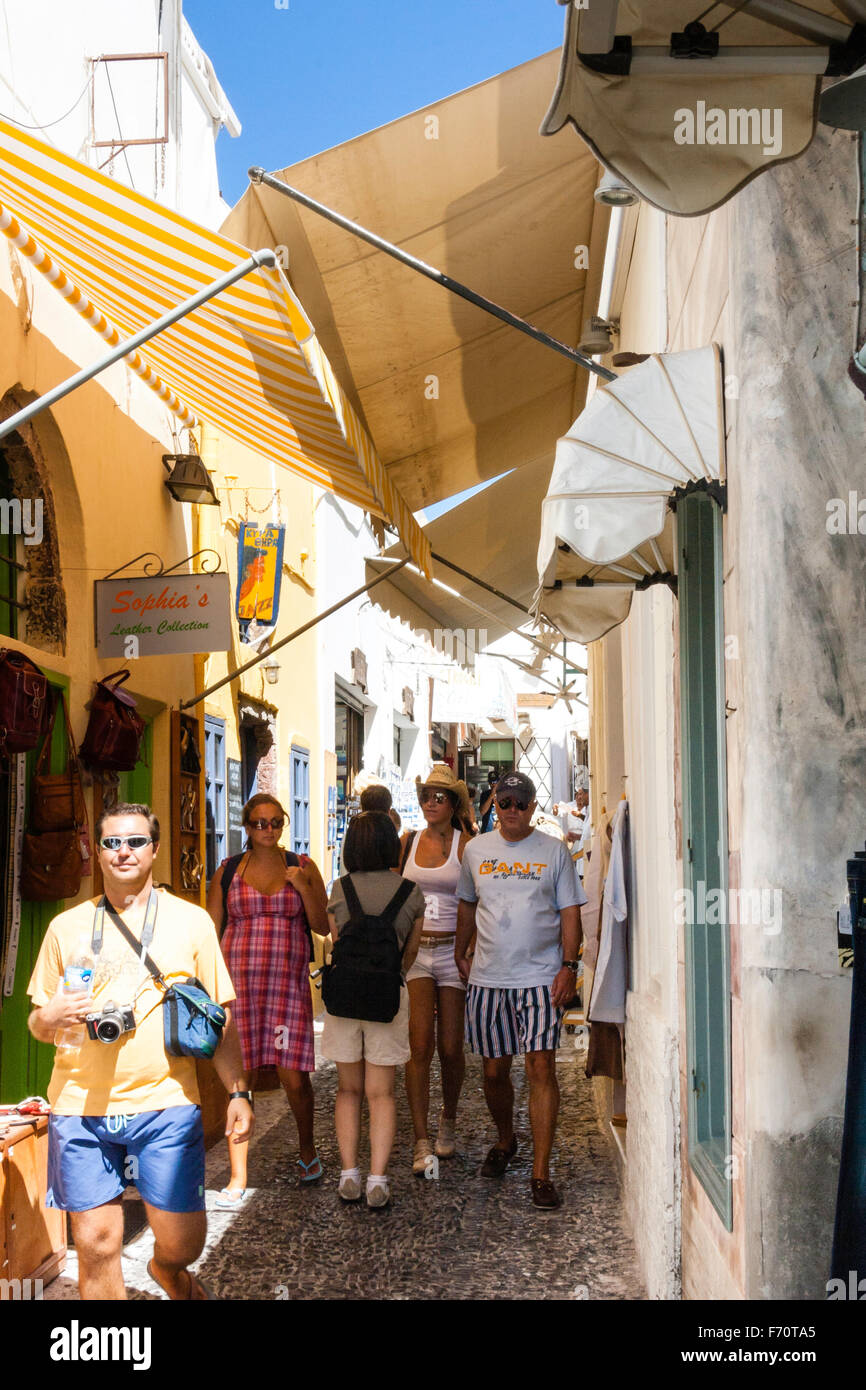 Santorin. Les touristes en se promenant dans la rue pavées typiques avec des magasins des deux côtés, et les frais généraux, les stores dans le vieux centre-ville de Fira. Banque D'Images