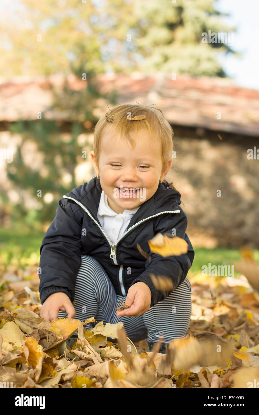 Mignon bébé âgé d'un an fille jouant avec les feuilles d'automne dans un parc Banque D'Images