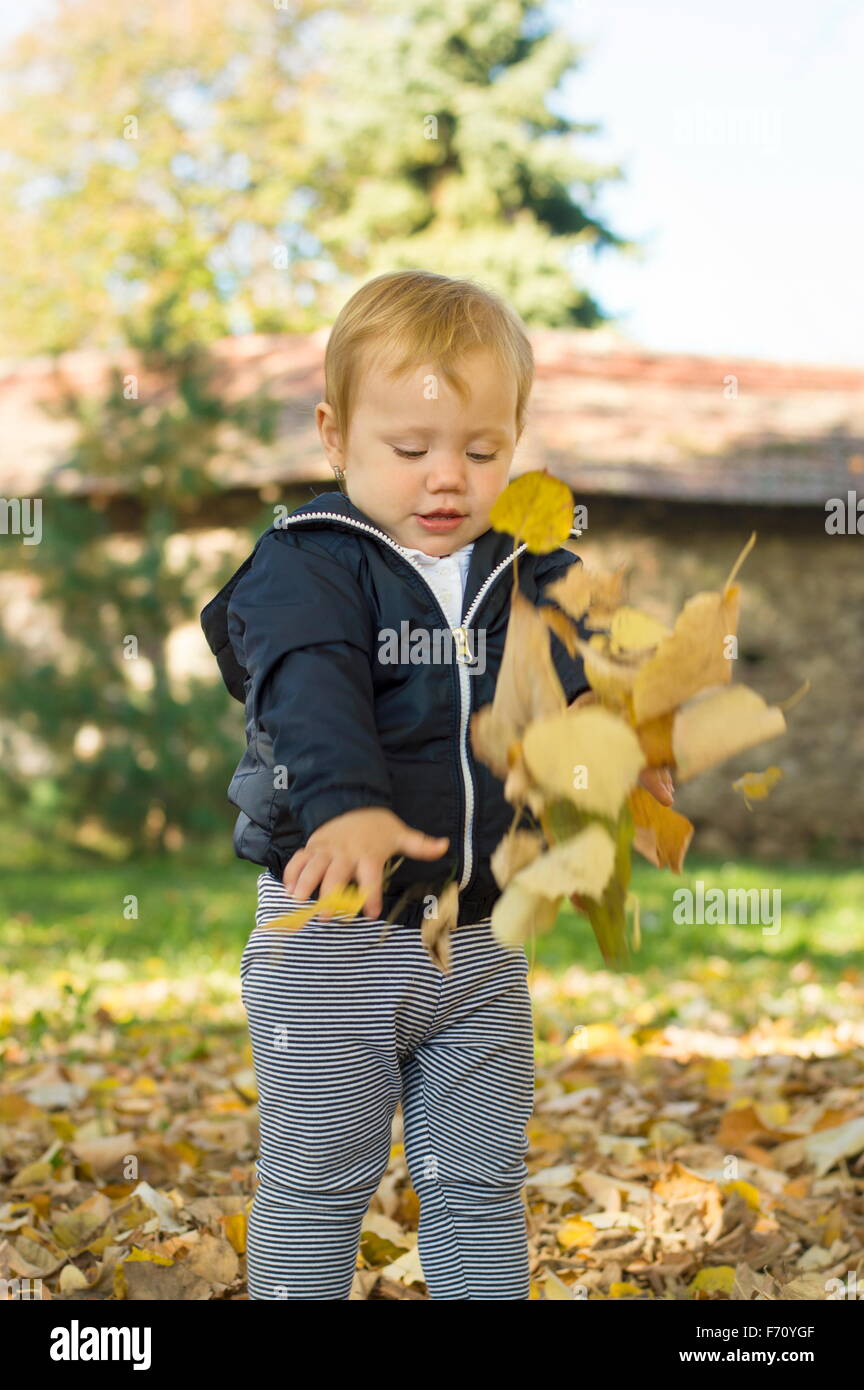 Mignon bébé âgé d'un an fille jouant avec les feuilles d'automne dans un parc Banque D'Images