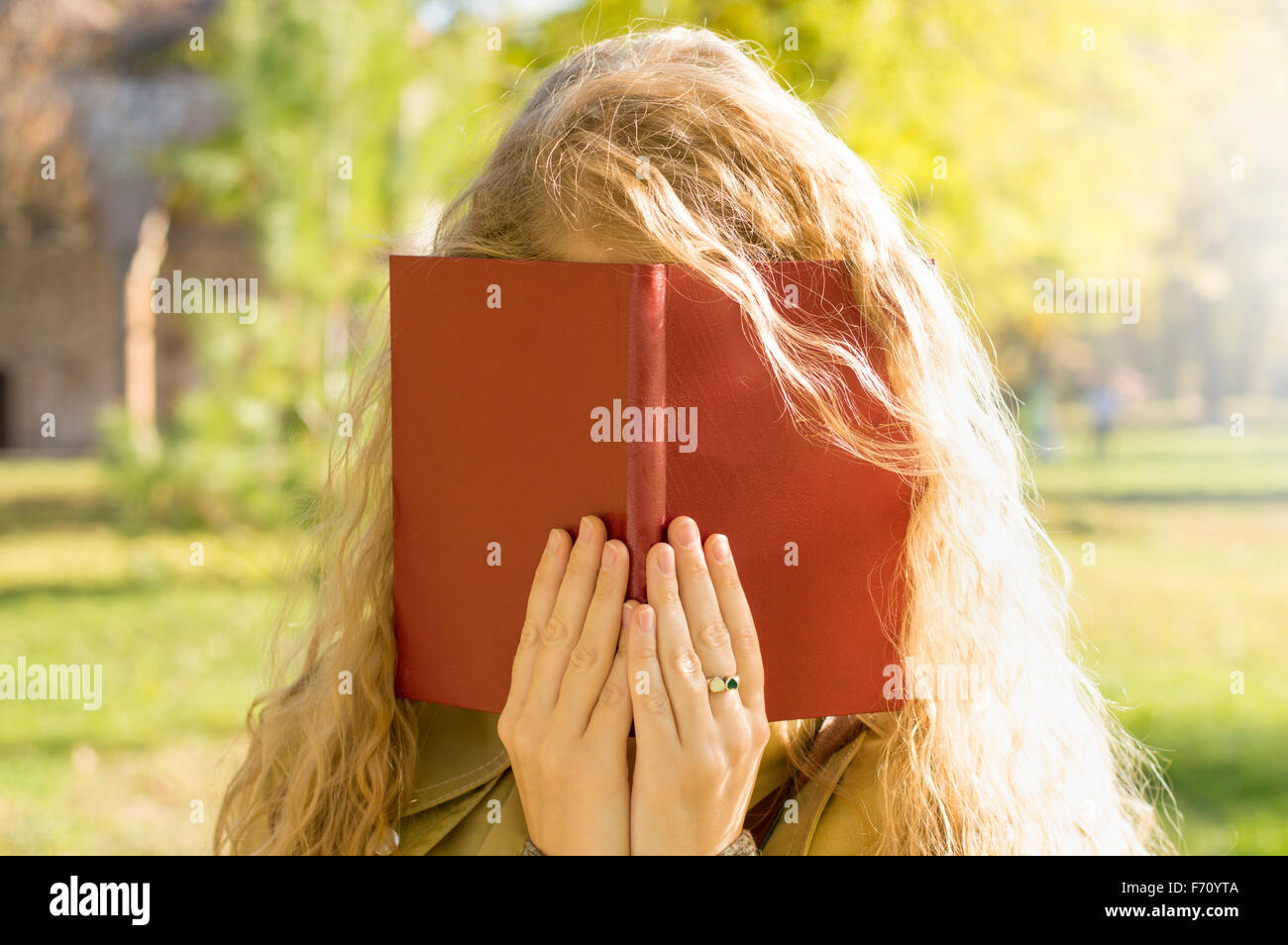 Fille blonde couvrant le visage avec un livre rouge dans un parc Banque D'Images