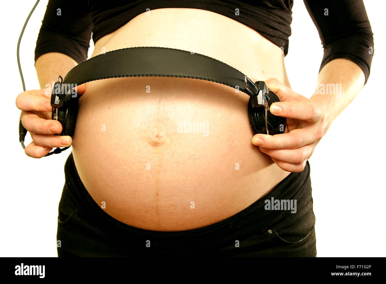 Les bras sur le ventre du ventre de maman enceinte holding écouteurs pour aimer la musique bébé fond blanc Banque D'Images