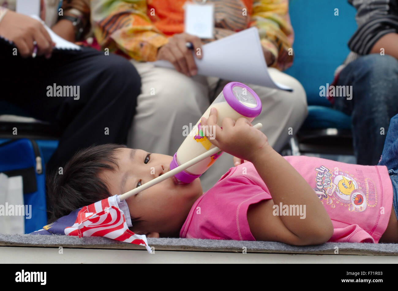 La petite fille de Malaisie se trouve sur la scène et de boire le lait d'un mamelon, tenant un drapeau de la Malaisie, Kuala Lumpur, Malaisie Banque D'Images