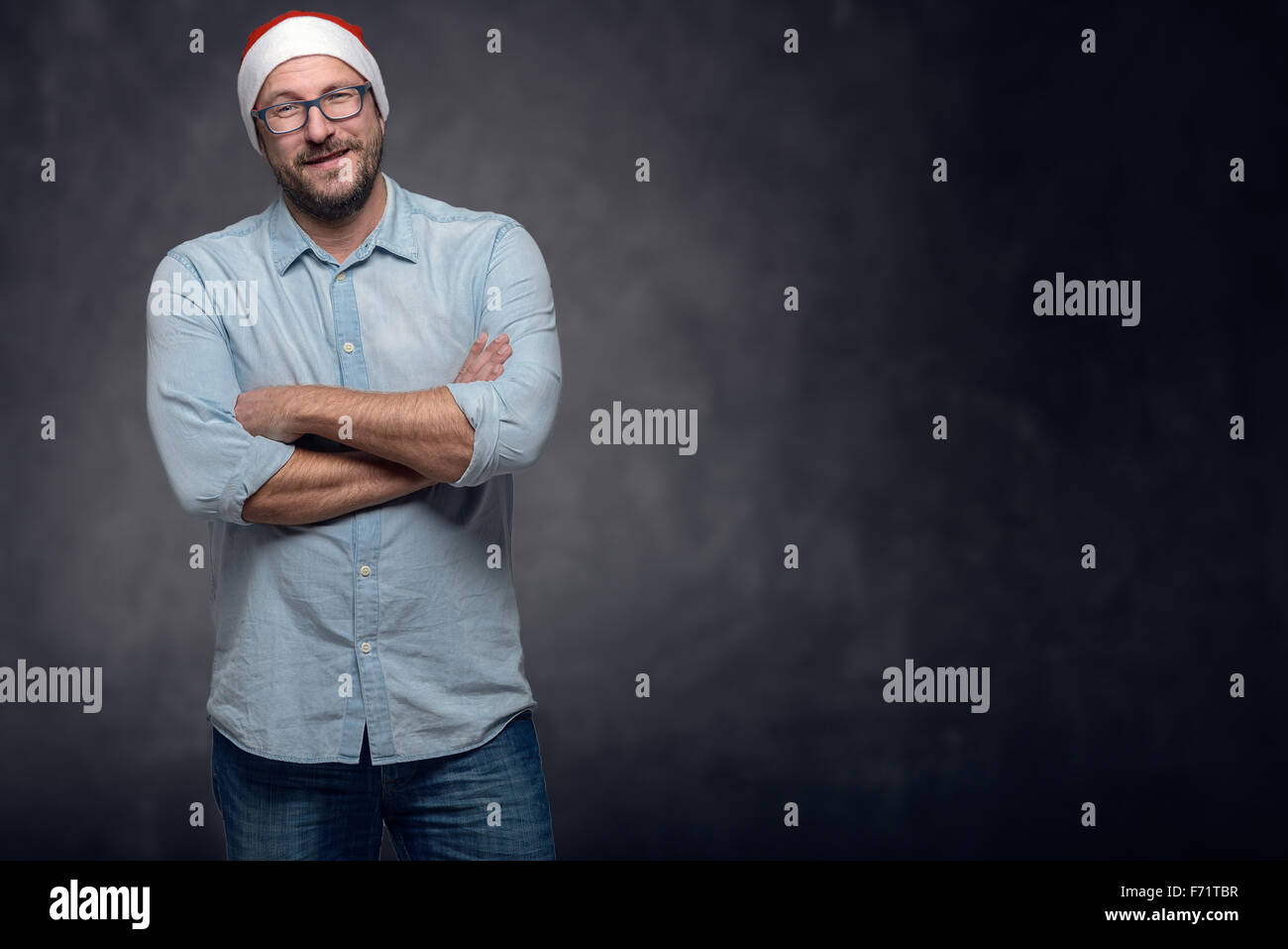 Trois quart d'un homme d'âge moyen, le port de Santa Clause Hat, souriant à la caméra, avec passage des bras sur sa poitrine, Aga Banque D'Images