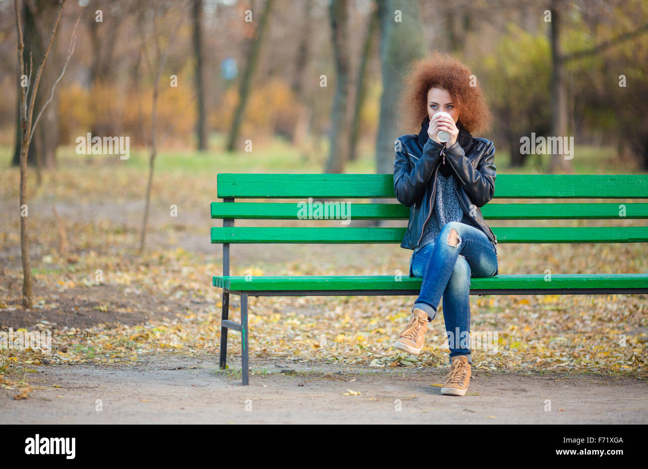 Portrait d'une jeune femme aux cheveux bouclés assis sur le banc et de boire du café en plein air Banque D'Images