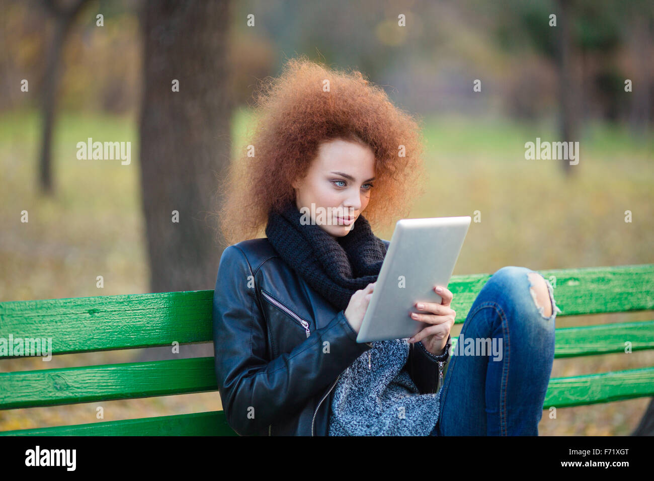 Portrait d'une belle femme avec des cheveux bouclés assis sur le banc et using tablet computer in autumn park Banque D'Images