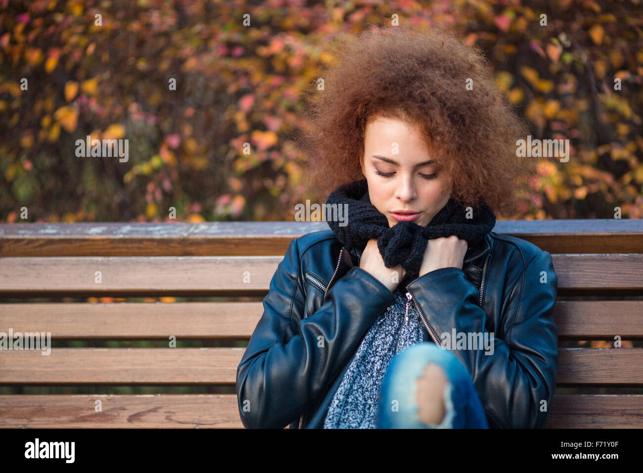 Portrait d'une jeune femme aux cheveux bouclés assis sur le banc du parc en automne Banque D'Images