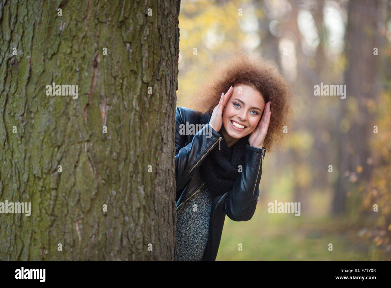 Portrait d'une femme souriante avec des cheveux bouclés, à l'arrière un arbre en automne park Banque D'Images