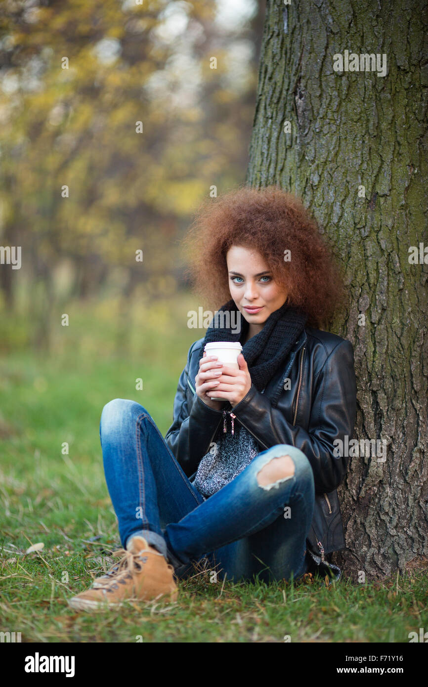 Portrait d'une belle femme avec les cheveux bouclés de boire du café sous l'extérieur de l'arbre Banque D'Images