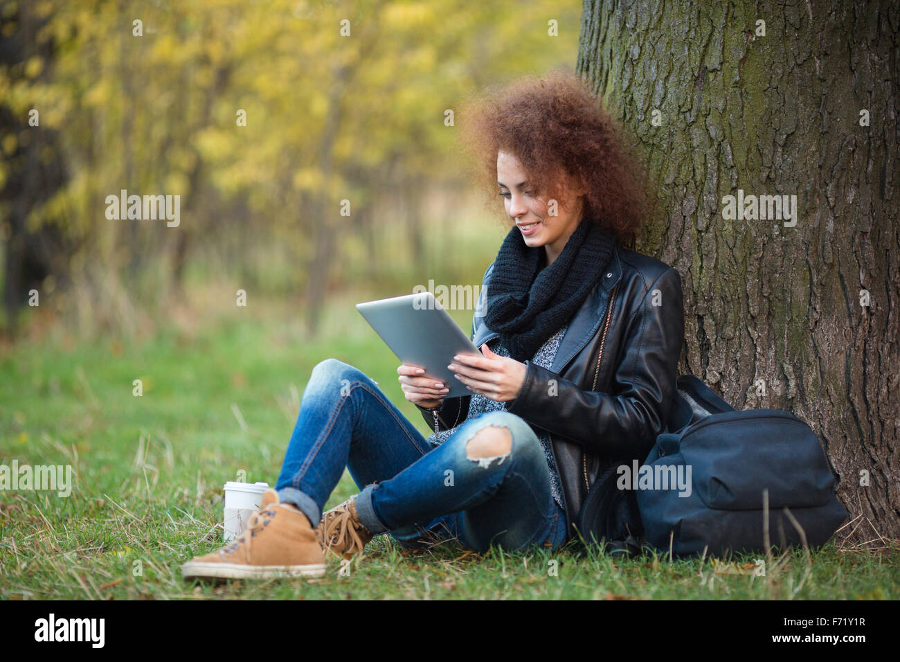 Portrait of a happy attractive woman avec les cheveux bouclés à l'aide de l'ordinateur tablette sous l'extérieur de l'arbre Banque D'Images