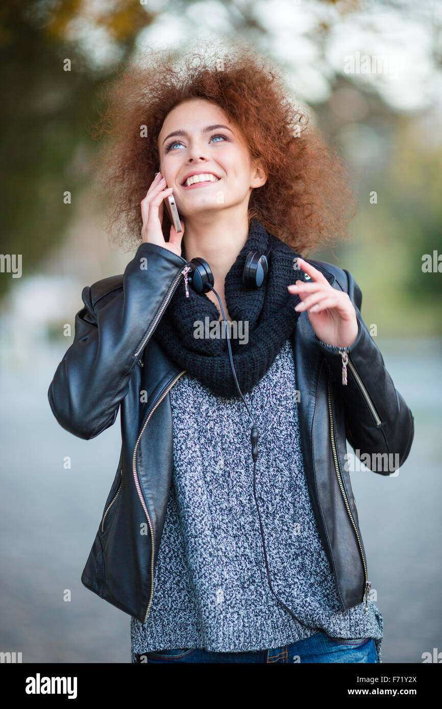 Portrait d'une femme souriante avec des cheveux bouclés à parler au téléphone et à la recherche jusqu'à l'extérieur Banque D'Images