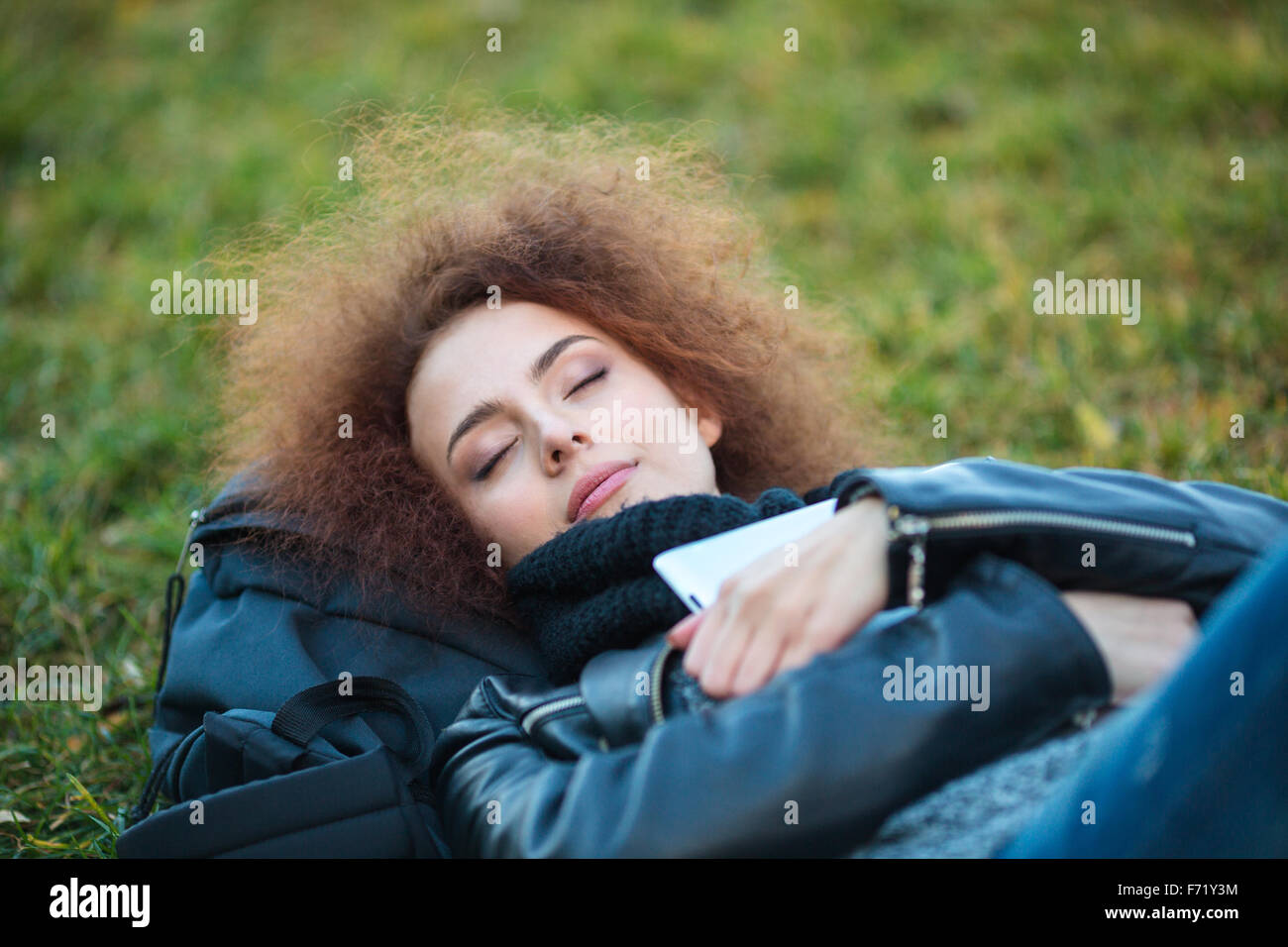 Portrait d'une jeune femme aux cheveux bouclés de dormir sur l'herbe verte à l'extérieur Banque D'Images