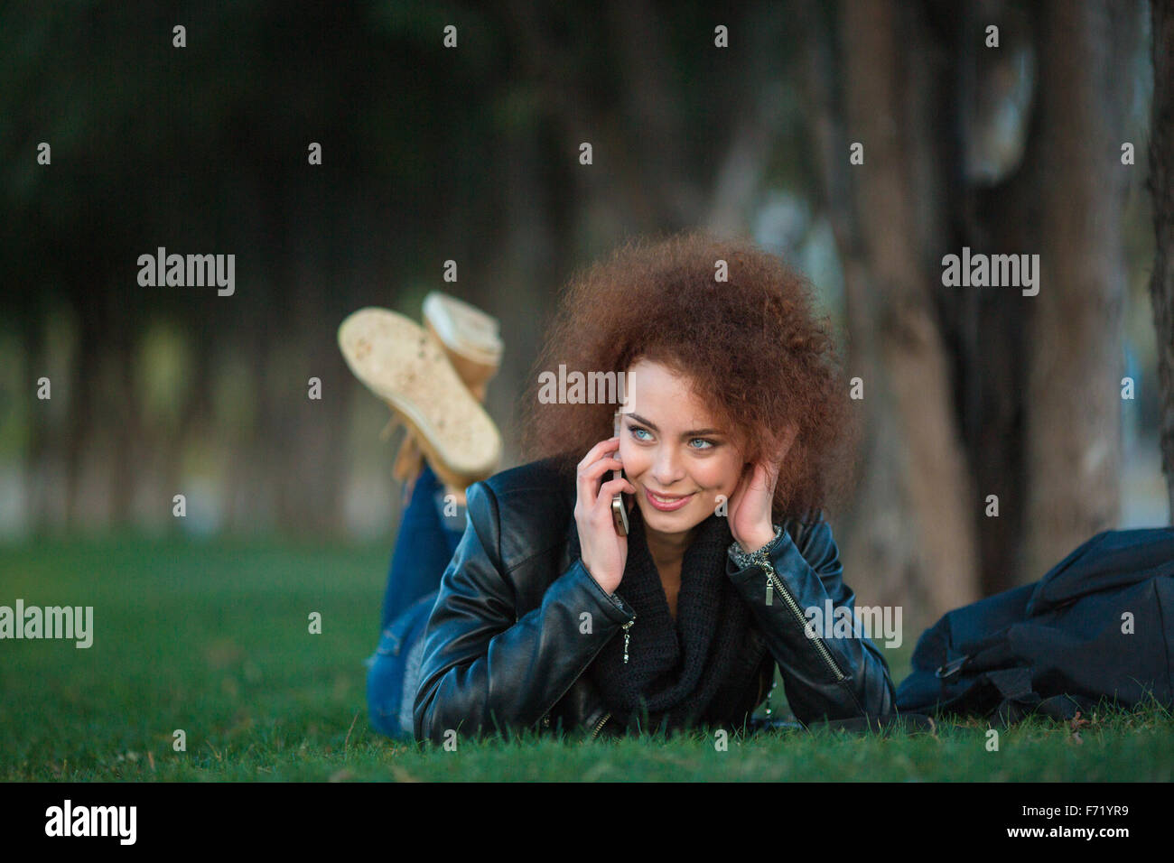 Portrait d'une femme heureuse avec des cheveux bouclés allongé sur l'herbe verte et à parler au téléphone à l'extérieur Banque D'Images