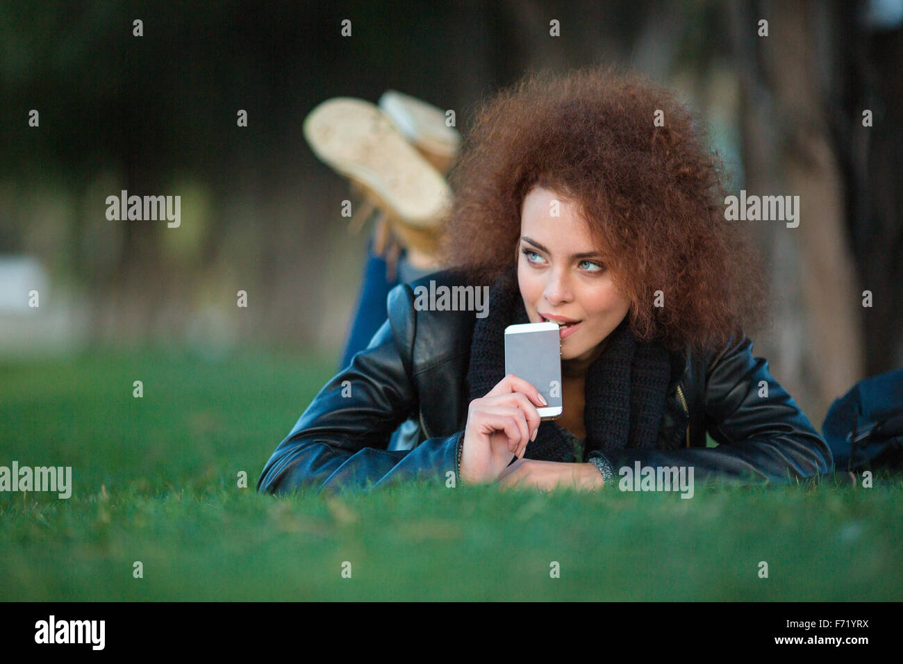 Portrait d'une femme avec les cheveux bouclés allongé sur l'herbe verte avec smartphone outdoors Banque D'Images