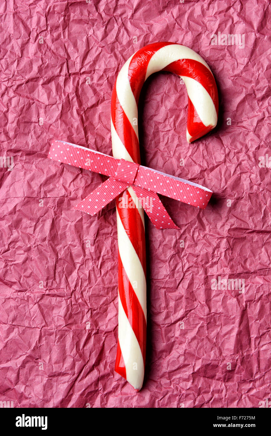 Libre d'une ancienne canne de Noël avec un noeud à pois. Format vertical sur papier froissé du papier de soie rouge. Banque D'Images