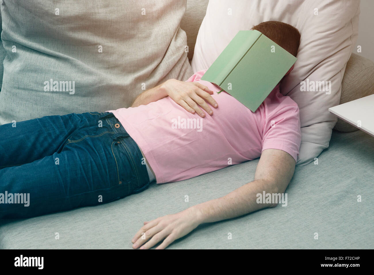 L'homme en jeans et tshirt dormir sur table avec le livre sur la tête Banque D'Images