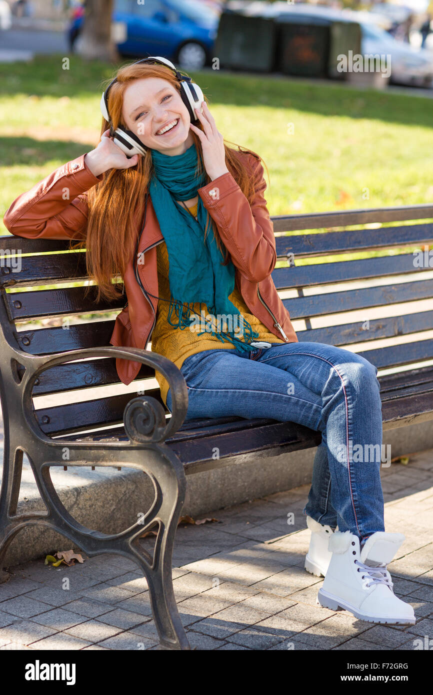 Portrait de jeune femme rousse heureux joyeux en veste de cuir, jeans,  écharpe lumineuse et des bottes blanches à écouter Photo Stock - Alamy
